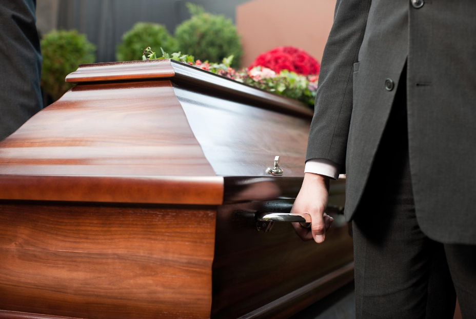 man in black suit holding a mahogany casket | Pre-planning vs traditional funeral planning | Overnight Caskets 